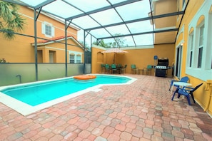 A covered outdoor swimming pool with a brick floor, surrounded by chairs and a grill area. - Terra Verde Resort 101 (Kissimmee)