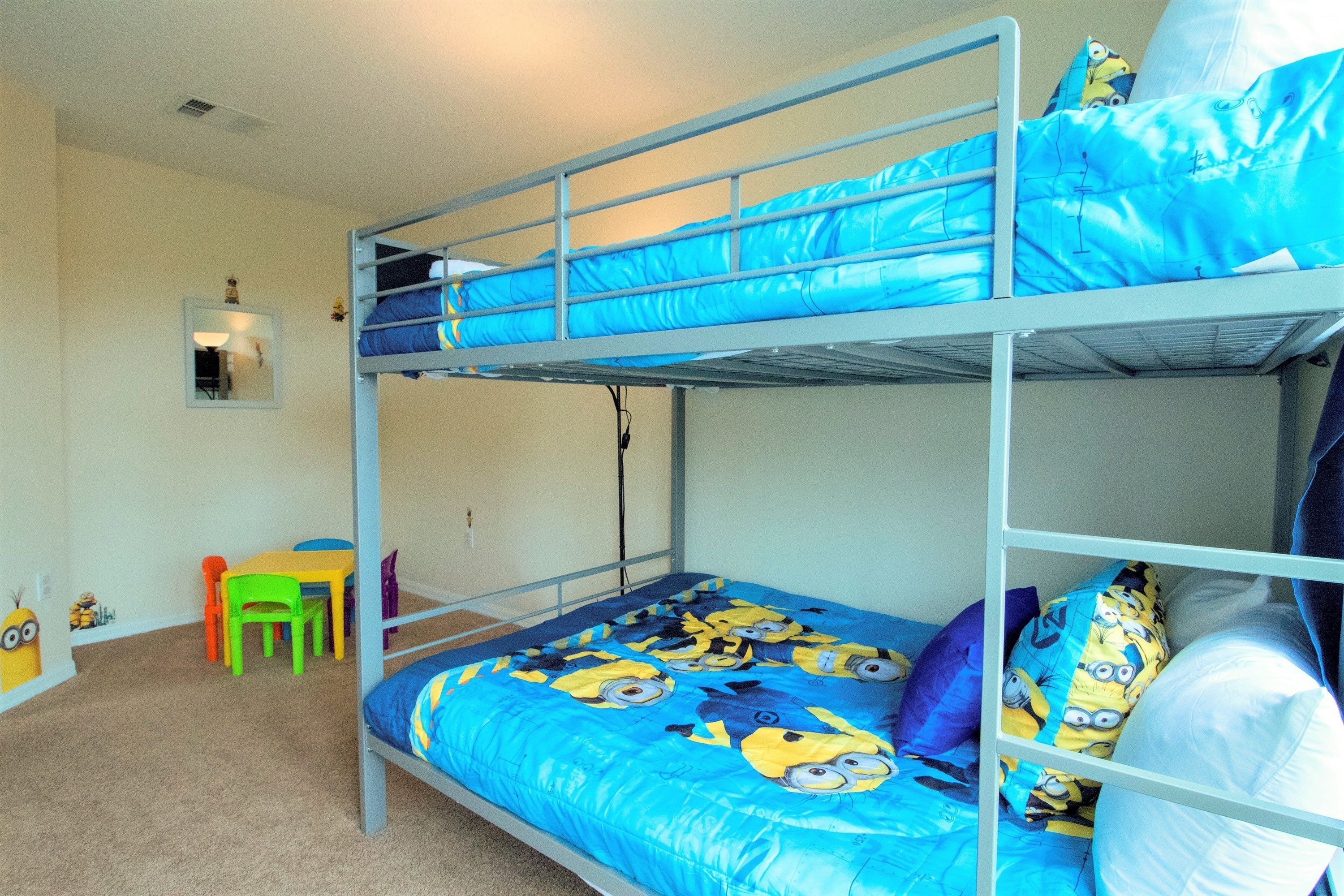 A bunk bed room with a Minion-themed bedspread, a small desk, and a chair.