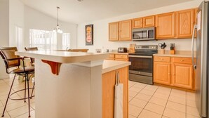 Una cocina moderna con armarios de madera, una isla central, electrodomésticos de acero inoxidable y un comedor con una silla y una mesa.