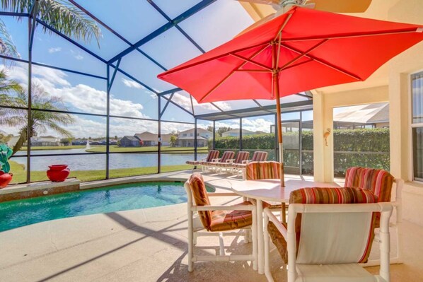 A covered outdoor area with a pool, lounge chairs, and a table with a red umbrella.
