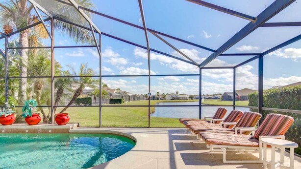 Zona de piscina techada con sillas de descanso y vista a un lago y casas al fondo.