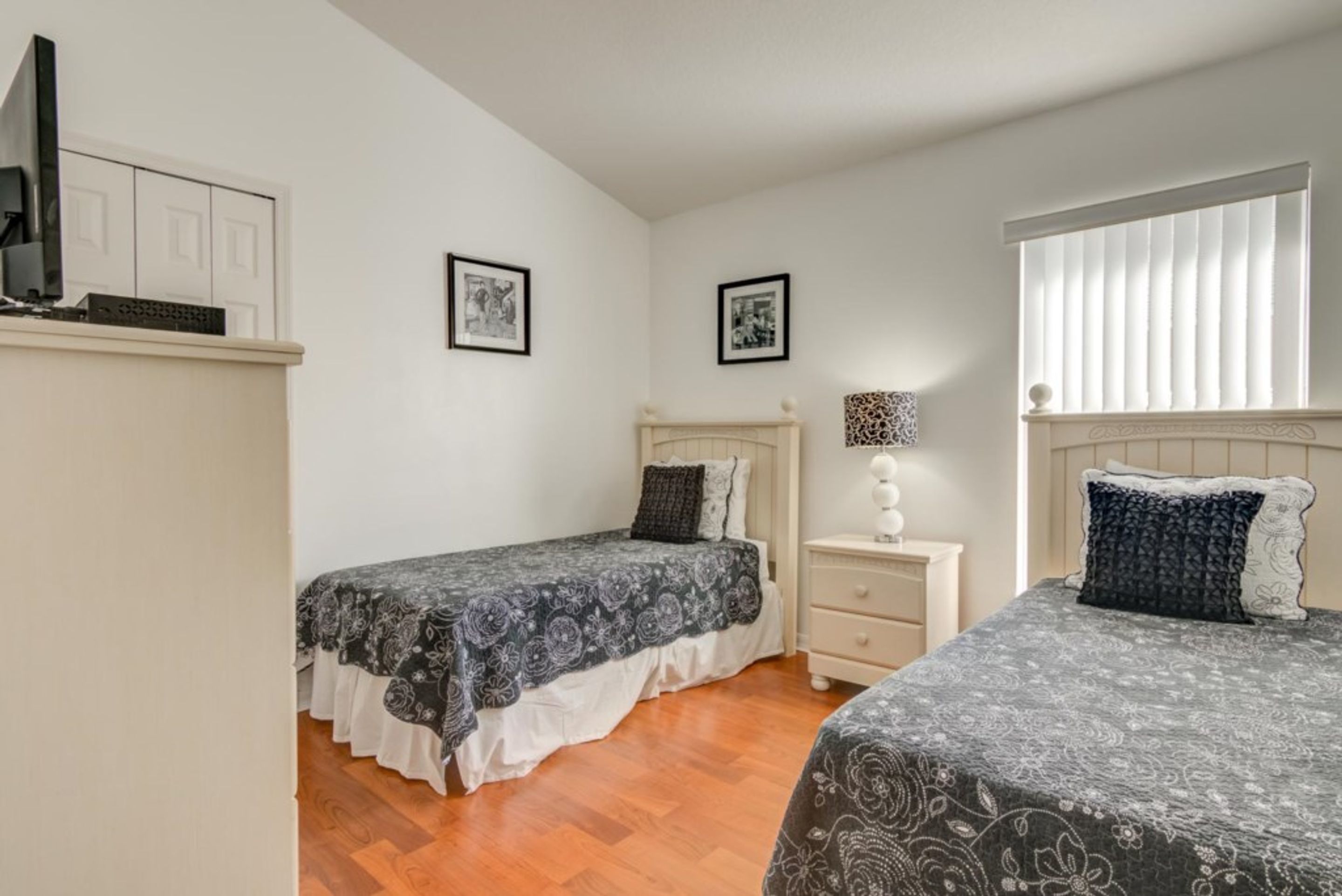A bedroom with two single beds, a nightstand with a lamp, and a TV on a shelf.
