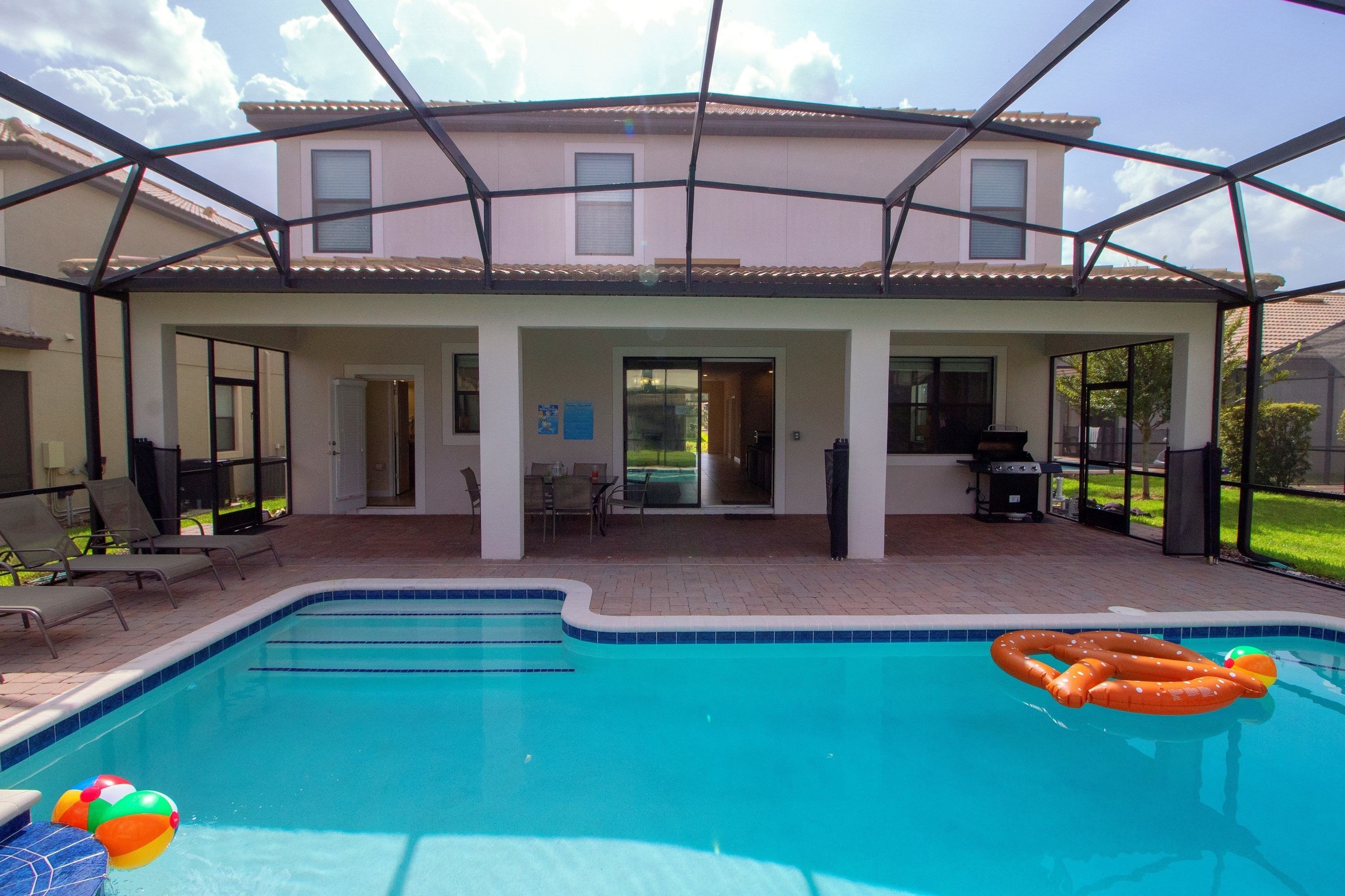 A covered outdoor swimming pool with a patio area, a barbecue grill, and a view of a residential building.