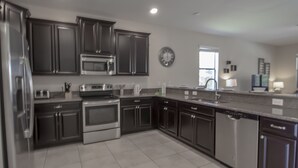 A modern kitchen with stainless steel appliances, dark cabinetry, and a tiled floor. - Champions Gate 1476 (Davenport)