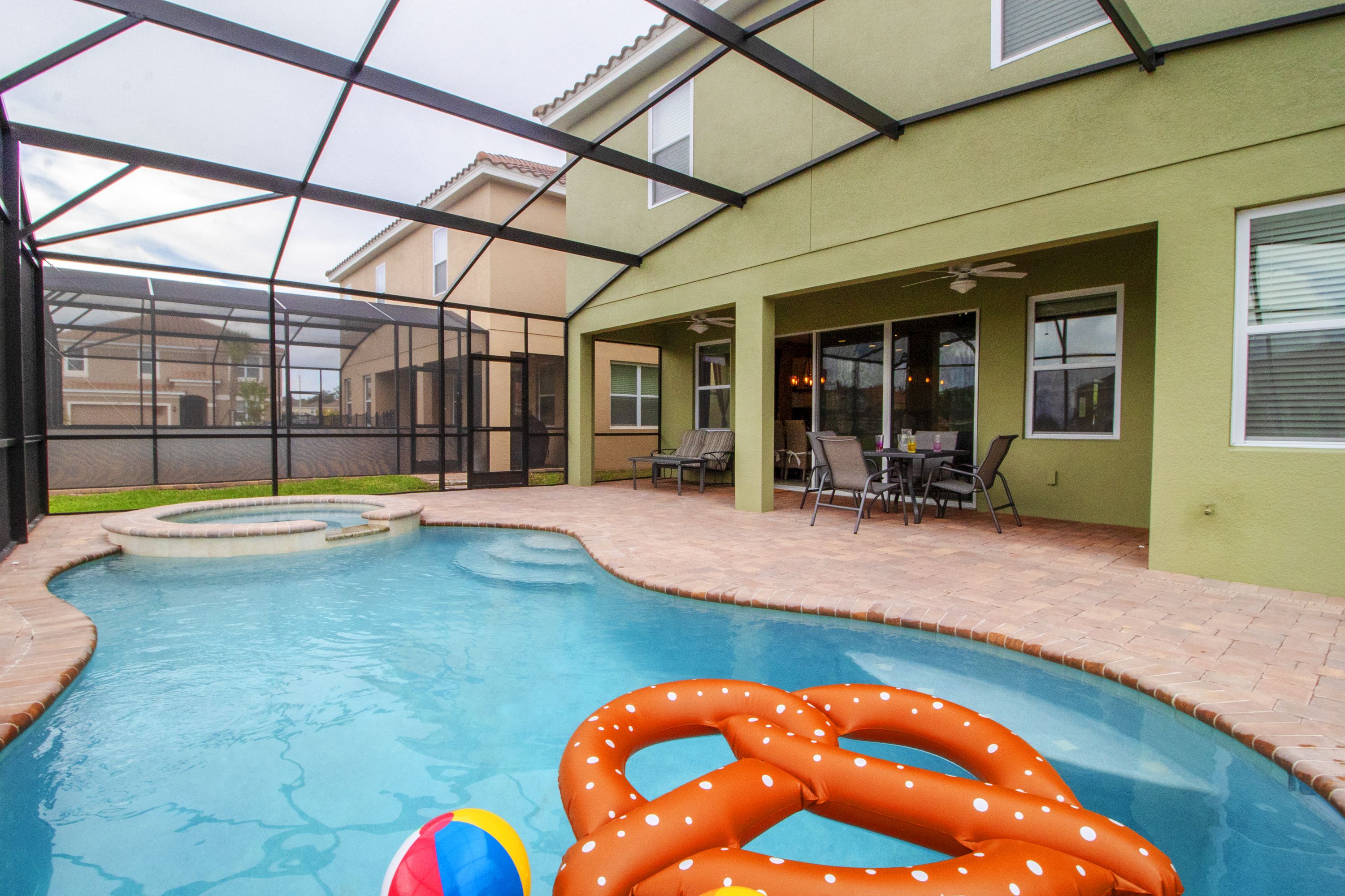A covered swimming pool with a hot tub, lounge chairs, and a patio area.