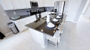 A modern kitchen with white cabinets, a stainless steel refrigerator, a microwave, and a sink.