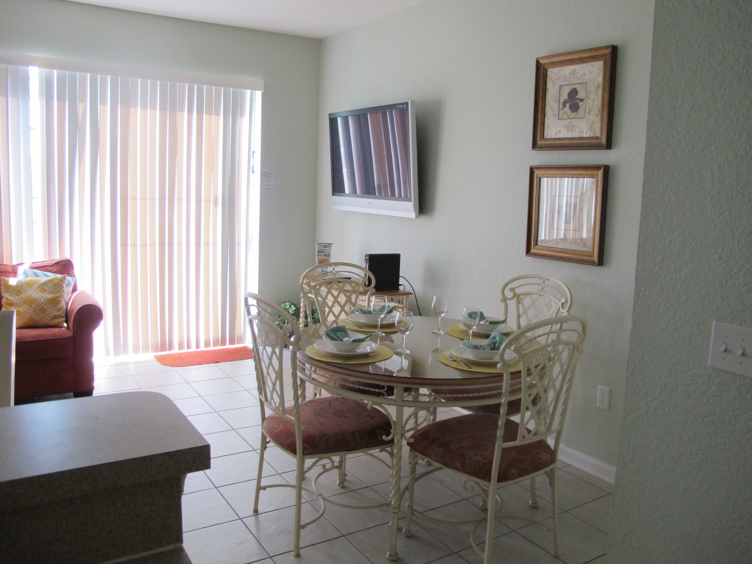 A dining area with a round table, white chairs, and a television mounted on the wall.