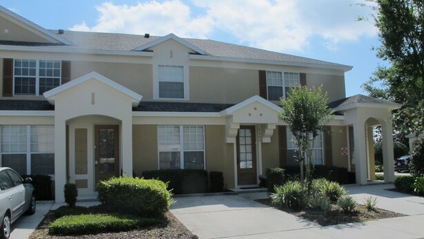 A row of townhouses with a uniform architectural style, featuring a central entrance with a small porch, and a driveway leading to the front of the building. - Windsor Hills 2503 (Kissimmee)