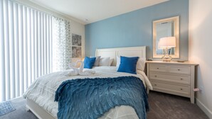 A bedroom with a bed, a dresser, a mirror, and a window with blinds.