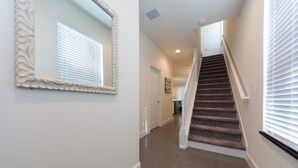 A hallway with a staircase, a mirror, and a door leading to another room.