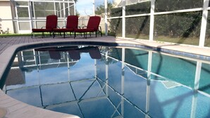 A swimming pool with a tiled deck, surrounded by glass walls and red chairs. - Chatham Park 2718 (Kissimmee)