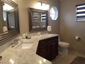 A bathroom with a marble sink, dark wooden cabinets, a toilet, and two large mirrors.