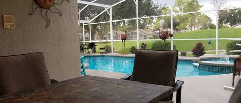 A covered patio with a pool, outdoor furniture, and a view of a residential neighborhood.