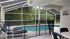 A covered outdoor pool area with lounge chairs and a table, surrounded by a safety fence.