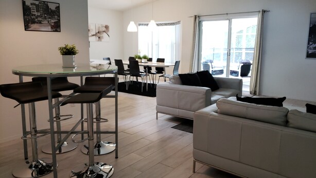 A modern living room with a sofa, a dining table with chairs, and a kitchen area in the background.