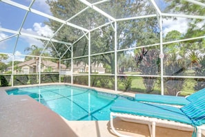 A covered swimming pool with lounge chairs and a view of surrounding houses and trees. - Southern Dunes 1501 (Haines City)