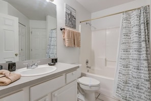A bathroom with a sink, mirror, towel rack, toilet, and shower curtain. - Southern Dunes 1501 (Haines City)