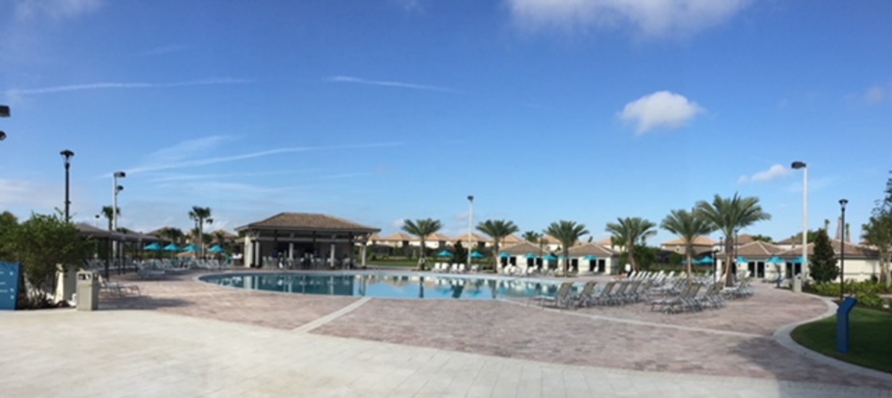 A resort pool area with lounge chairs, a covered pavilion, and palm trees.
