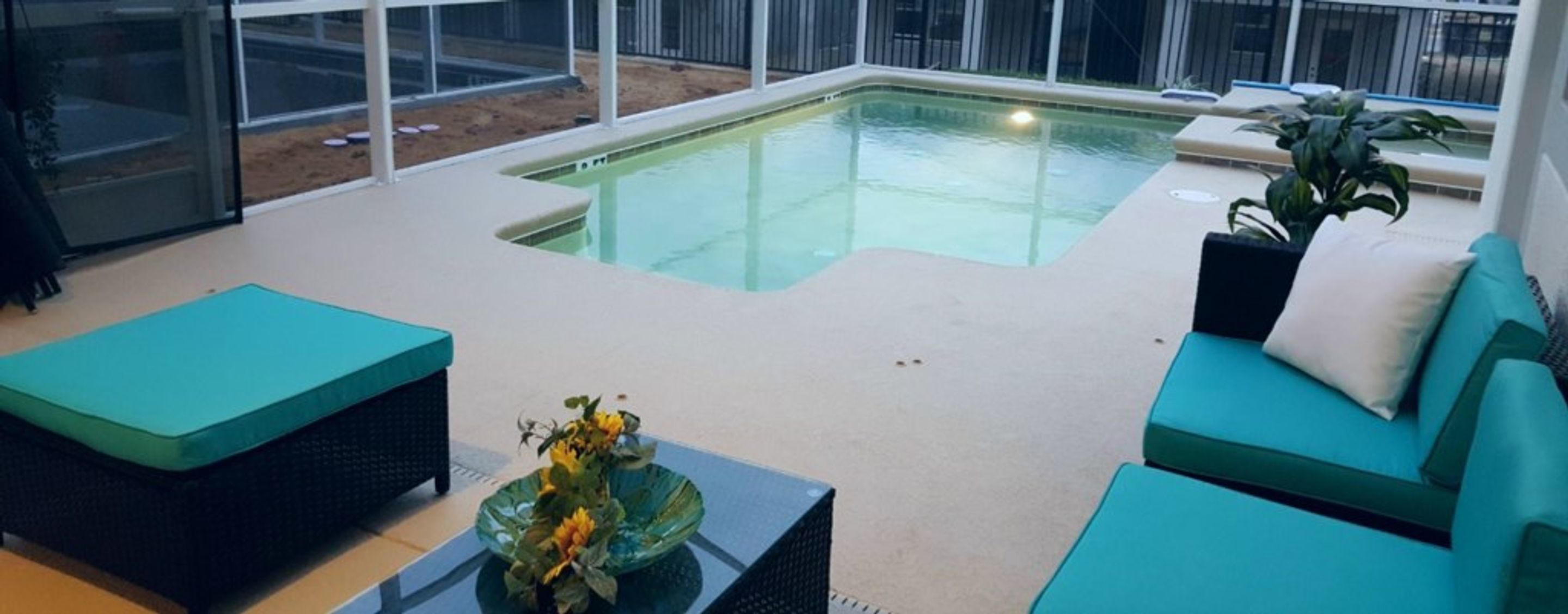Ein Poolbereich mit Glasverkleidung, smaragdgrünen Sitzmöbeln und einem Glastisch mit Blumenarrangement.