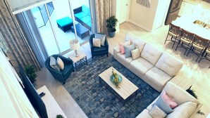 A spacious living area with a sofa, armchair, and coffee table. There is a dining area with chairs and a table.
