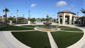A courtyard with a central fountain, surrounded by a well-maintained lawn and a building with a tiled roof.