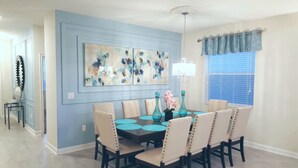A dining area with a blue accent wall, a chandelier, and a window with blue curtains.