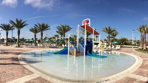 A water park with a central play structure, palm trees, and lounge chairs.