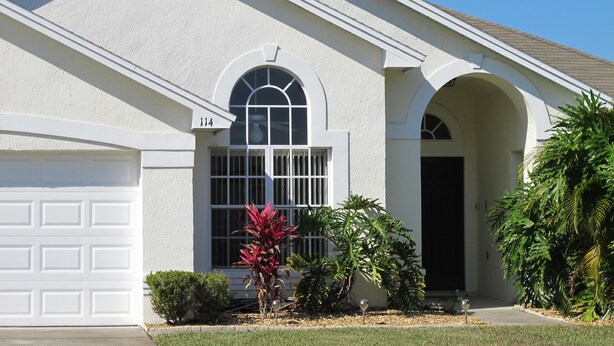 A single-story house with a white exterior, a garage door, and a large arched window. - Country Creek Estate 114 (Kissimmee)