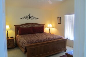 A bedroom with a wooden bed, two bedside tables with lamps, a decorative wall piece, and a window with blinds. - Country Creek Estate 114 (Kissimmee)