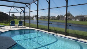 A pool with clear water, surrounded by a covered area with chairs and a view of a canal and houses. - Country Creek Estate 114 (Kissimmee)