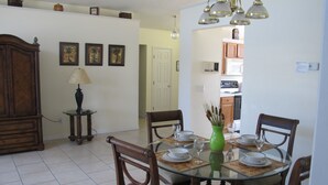 A dining area with a glass table, four chairs, a green vase, and a lamp. - Country Creek Estate 114 (Kissimmee)