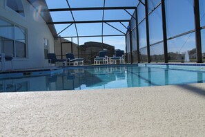 An indoor swimming pool with clear blue water, surrounded by a covered area with chairs and a view of the outside. - Country Creek Estate 114 (Kissimmee)