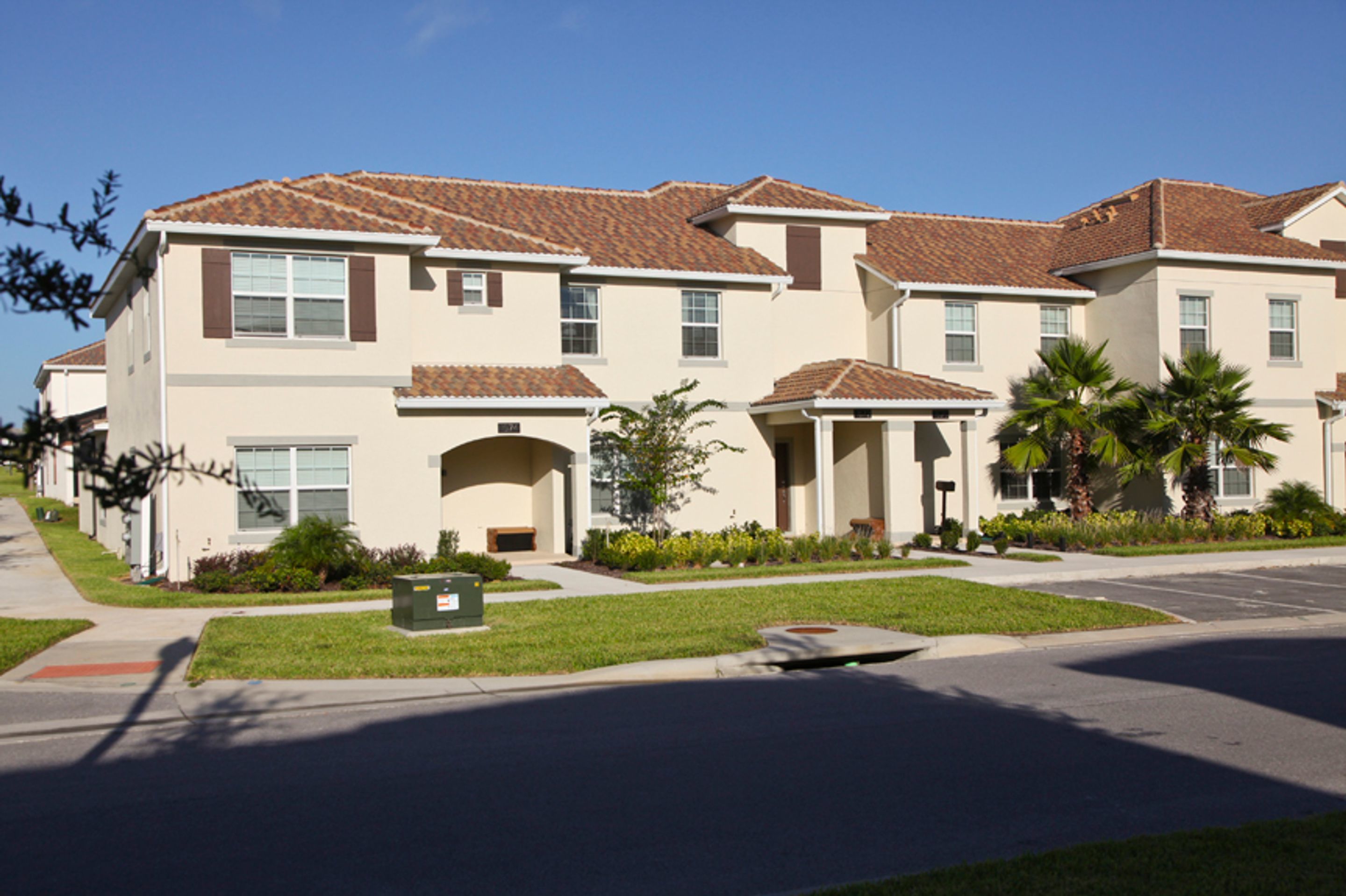 A row of townhouses with a consistent architectural style, featuring a central entrance with a covered porch, and a well-maintained lawn and garden area.