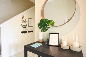 A hallway with a coat rack, a large mirror, a potted plant, a framed picture, and candles on a table. - Champions Gate 1570 (Davenport)