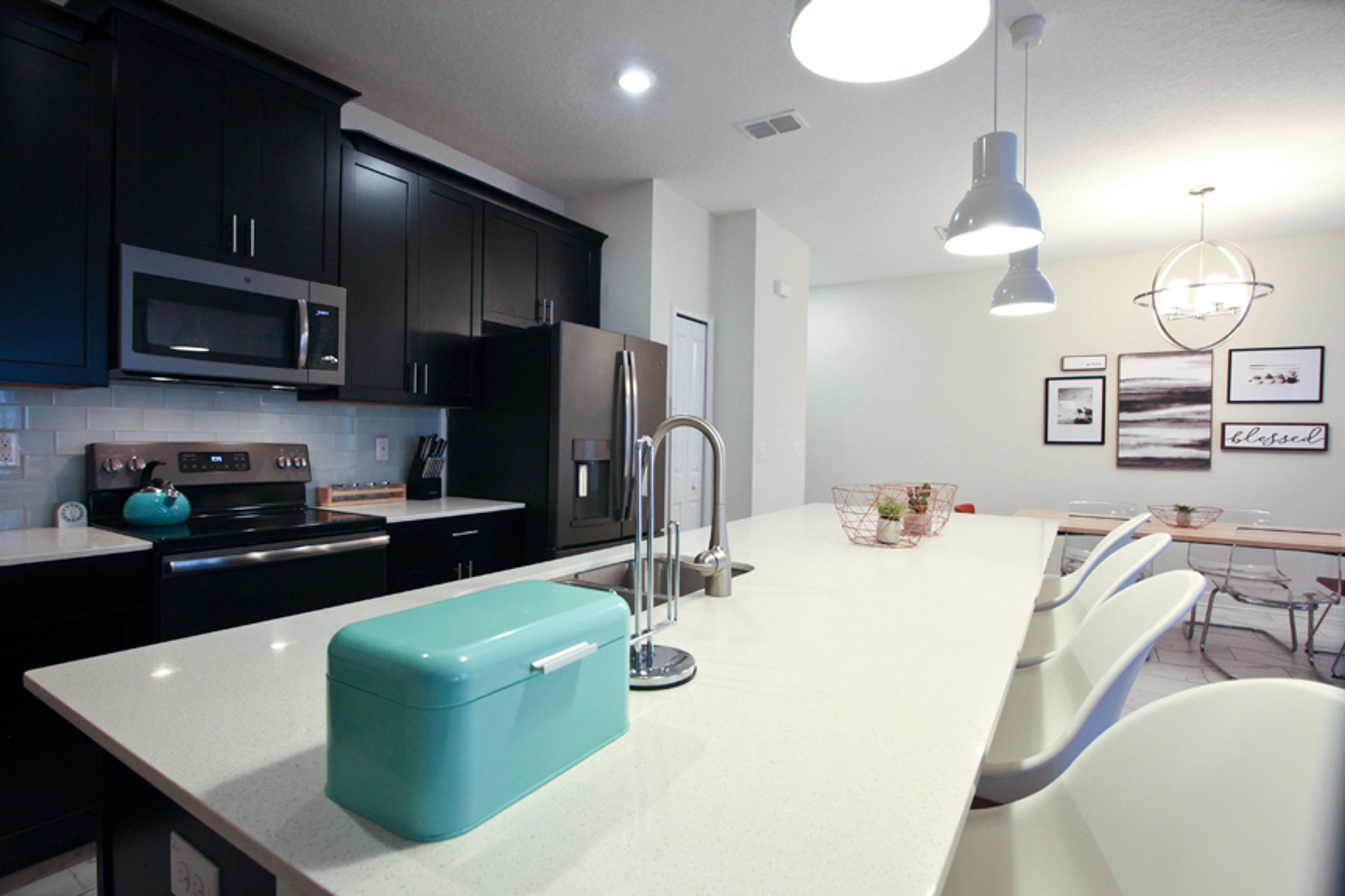 A modern kitchen with dark cabinets, a stainless steel microwave, a refrigerator, and a teal-colored appliance on the counter.