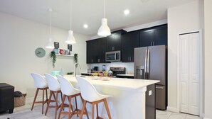 A modern kitchen with dark cabinets, a stainless steel refrigerator, and a white island with bar stools. - Champions Gate 1570 (Davenport)