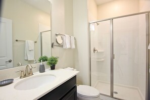 A bathroom with a sink, mirror, and a glass-enclosed shower. - Champions Gate 1570 (Davenport)