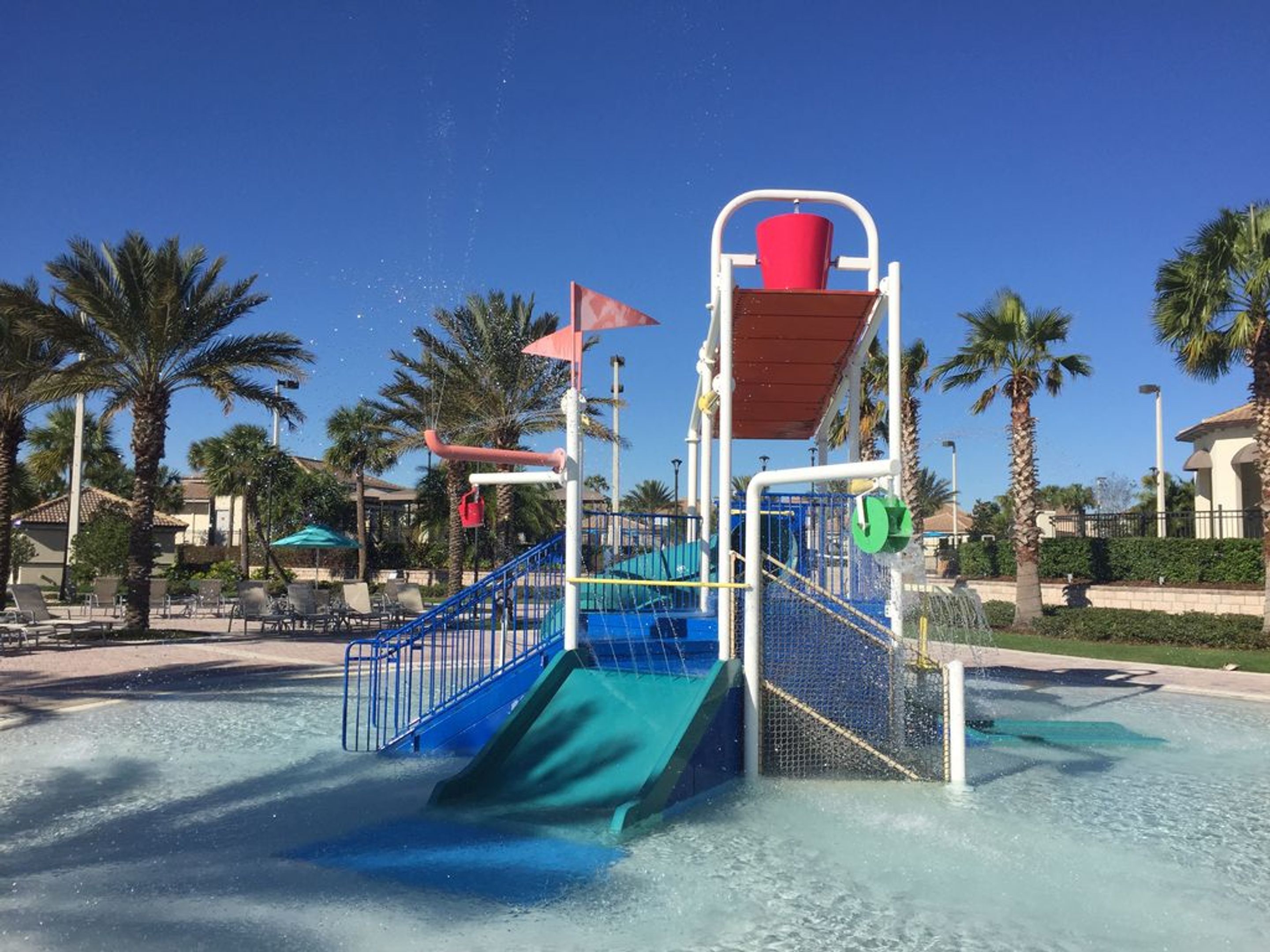 Un espace de jeux aquatiques avec des toboggans et des jets d’eau, entouré de palmiers et de chaises longues.