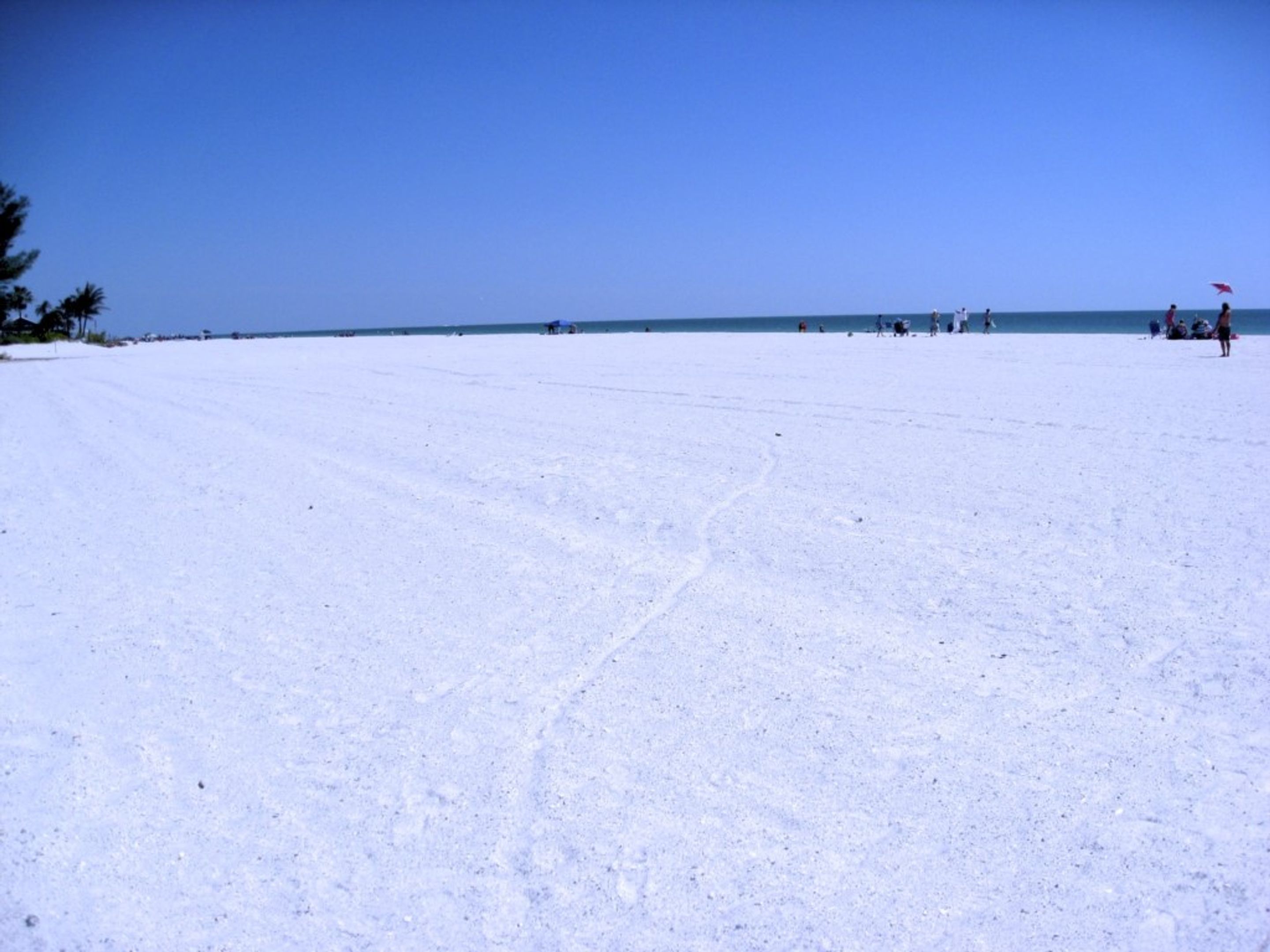 A wide, open beach with a clear sky and calm sea.
