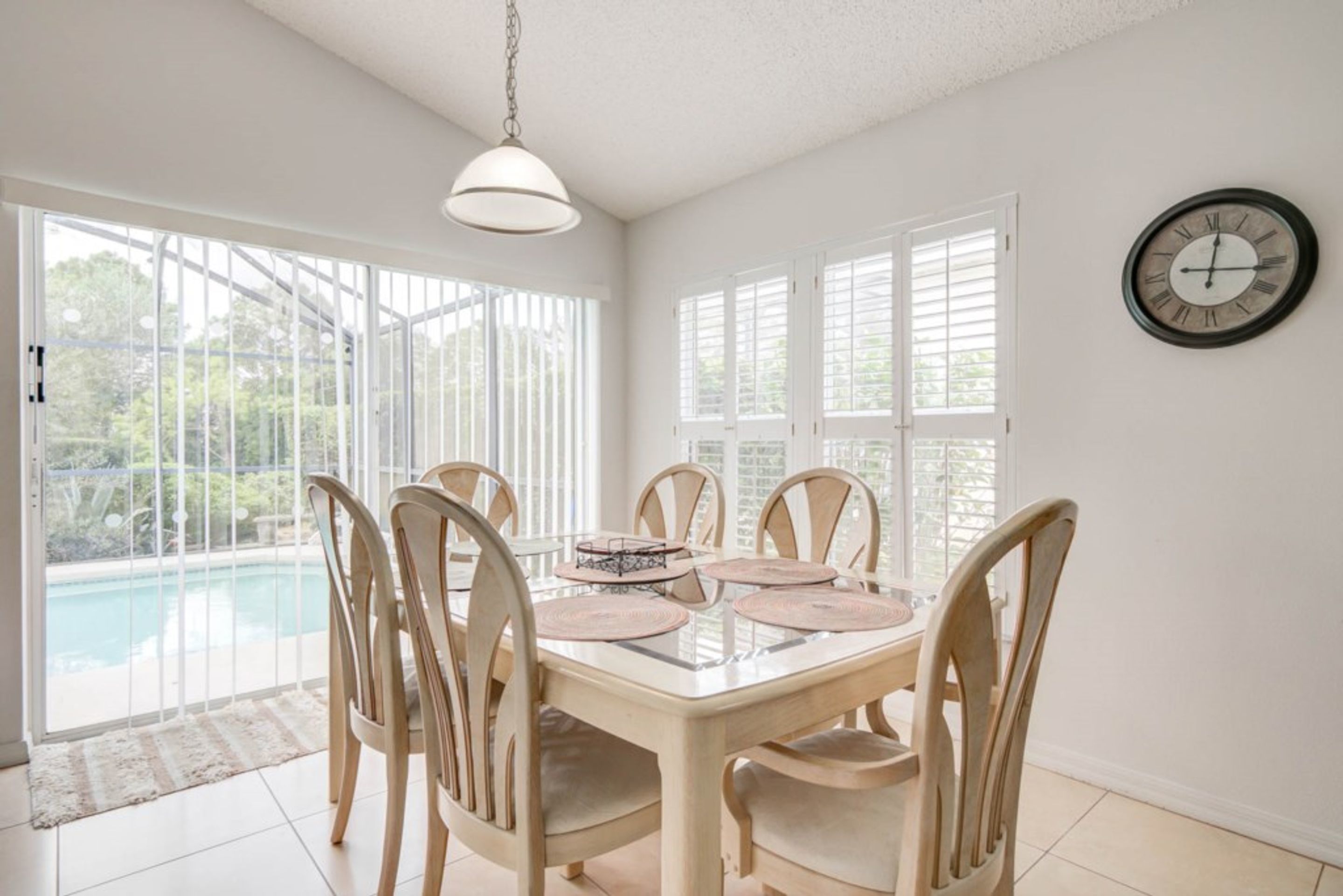 A dining area with a glass table, wooden chairs, and a clock on the wall.