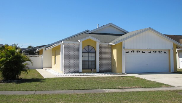 A single-story house with a garage, a small front yard, and a palm tree. - Indian Wells 3120 (Kissimmee)