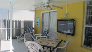 A sunlit patio with a table and chairs, a ceiling fan, and a TV mounted on the wall. - Indian Wells 3120 (Kissimmee)
