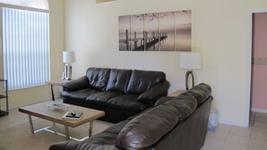 A living room with a black leather sofa, a coffee table, a lamp, and a wall-mounted 'WELCOME' sign. - Indian Wells 3120 (Kissimmee)