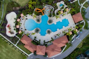 An aerial view of a resort with a large central pool, multiple smaller pools, and a water slide.