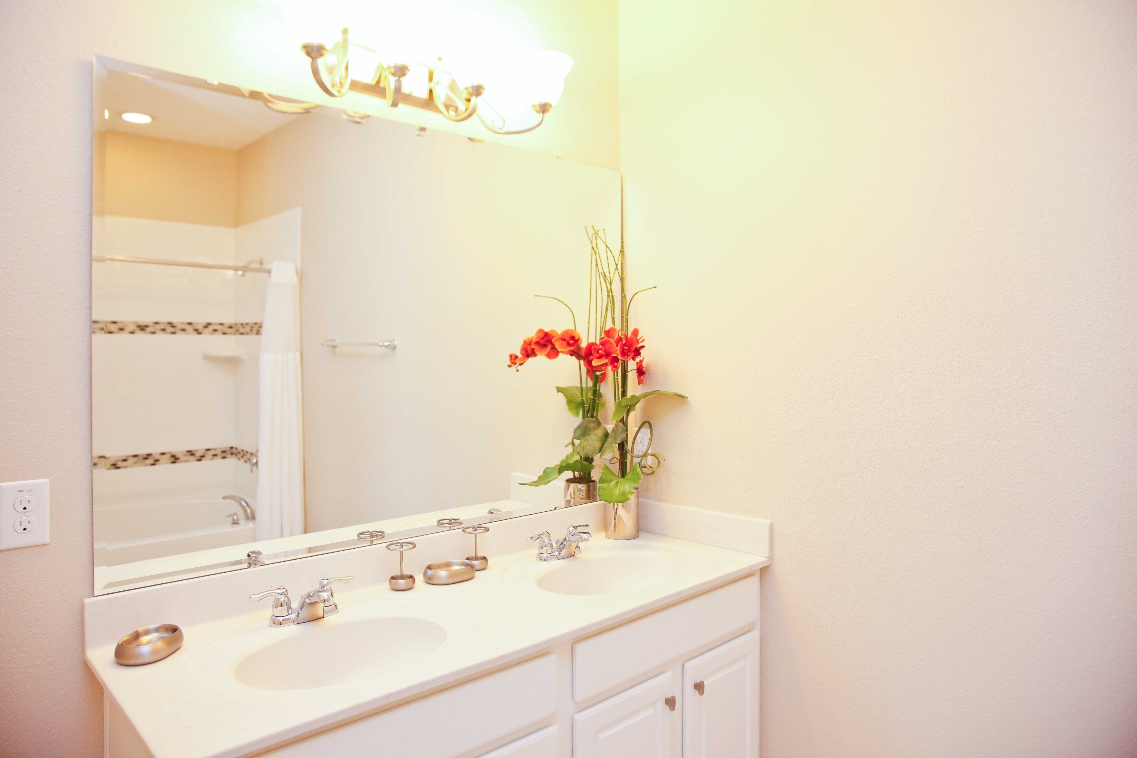 A bathroom with a double sink, a large mirror, and a vase with flowers.