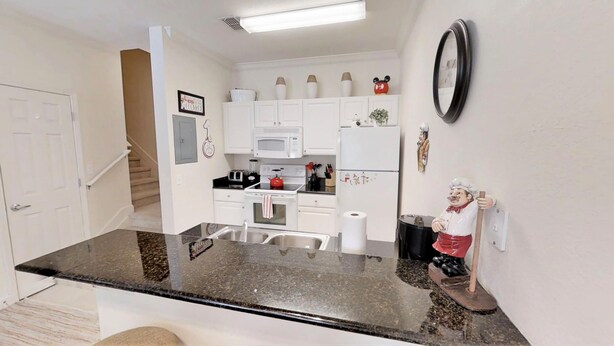 A compact kitchen with white cabinets, a microwave, a stove, and a refrigerator. There's a small statue of a chef on the counter.