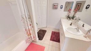 A bathroom with a white sink, mirror, and two towel racks. There are two towels on the floor and a shower curtain with a floral pattern.
