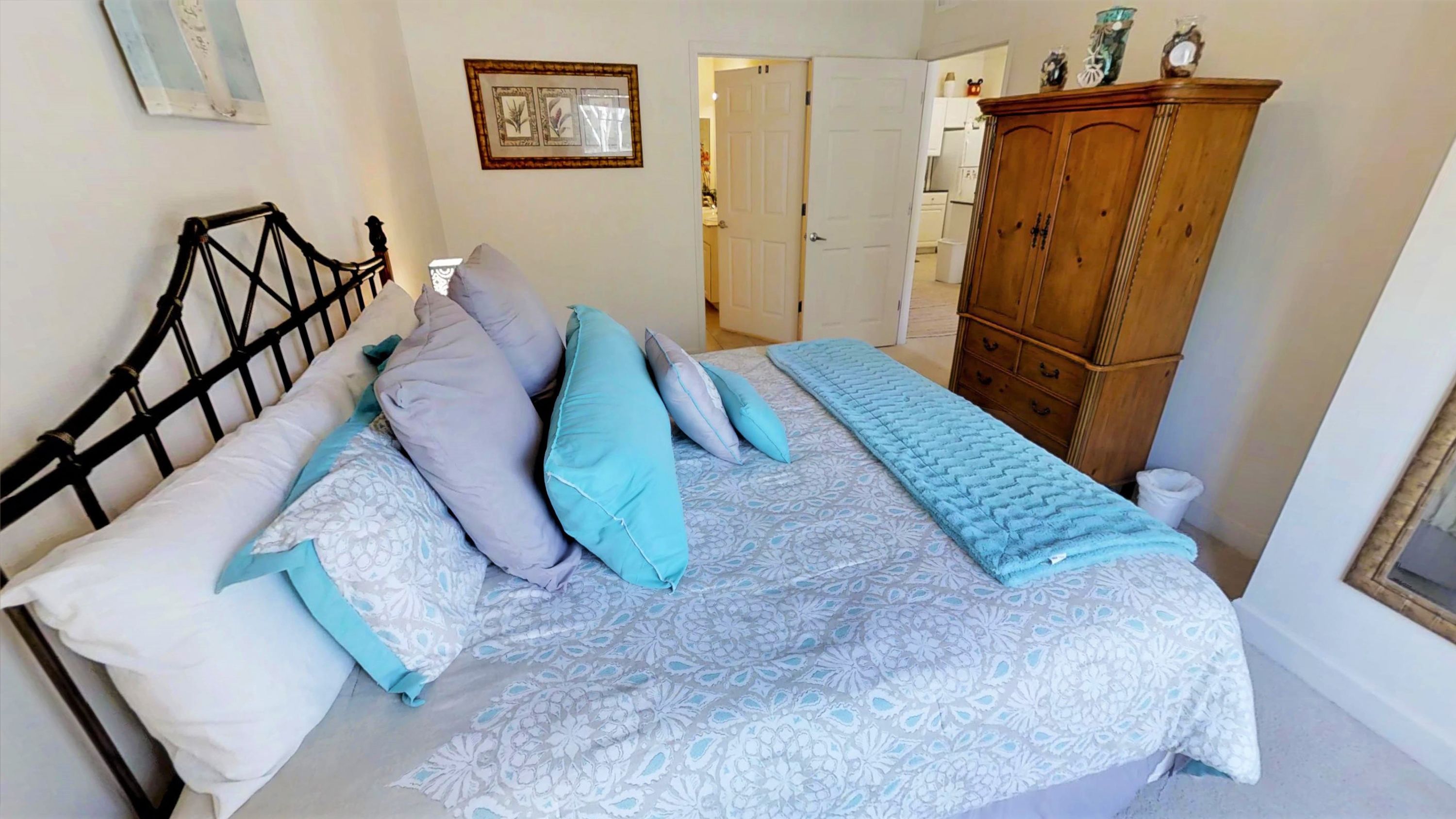 Una camera da letto con un letto, cuscini, un armadio in legno e una porta che dà su un bagno.