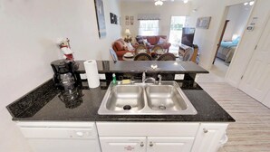 A kitchen with a black countertop, stainless steel sink, and white cabinets. There is a coffee maker, a roll of paper towels, and a bottle of dish soap on the counter.