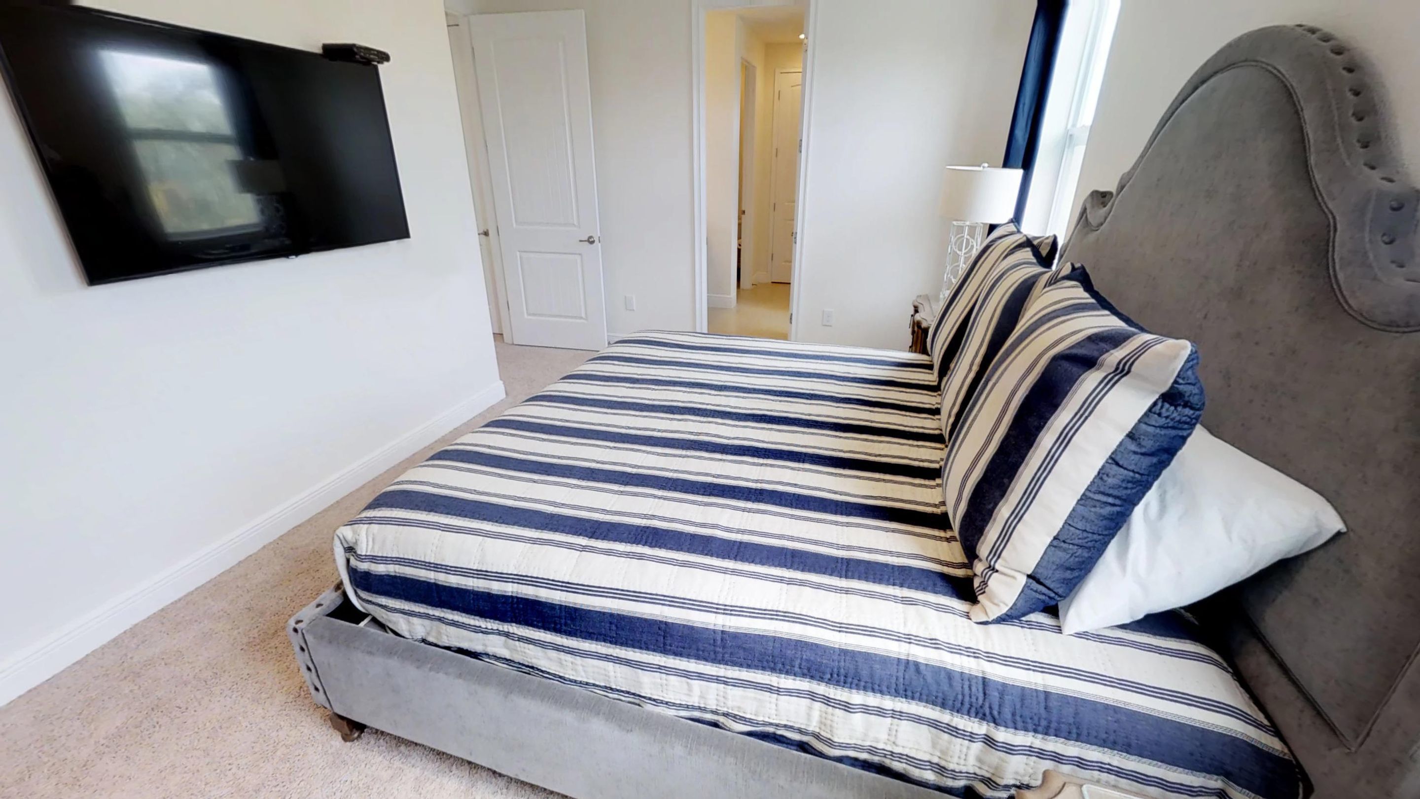 Un dormitorio con una cama, televisión instalada en la pared y una puerta que conduce a otra habitación.